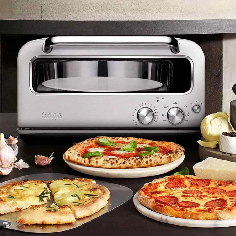 Sage Pizzaiolo sur un plan de travail, devant une margherita, une pizza blanche et une pizza pepperoni