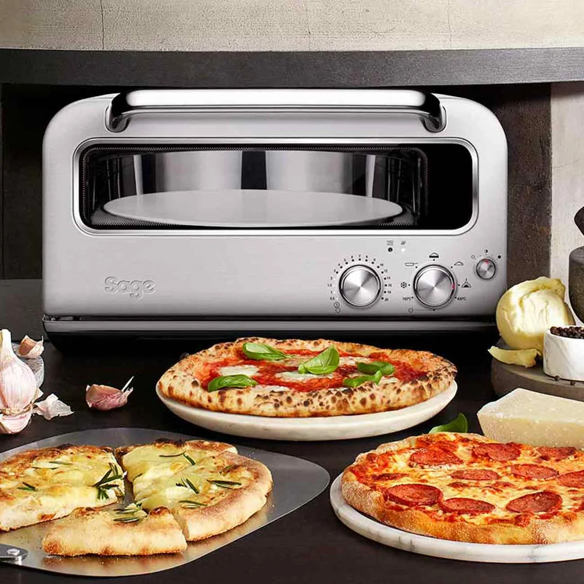 Sage Pizzaiolo sur un plan de travail, devant une margherita, une pizza blanche et une pizza pepperoni