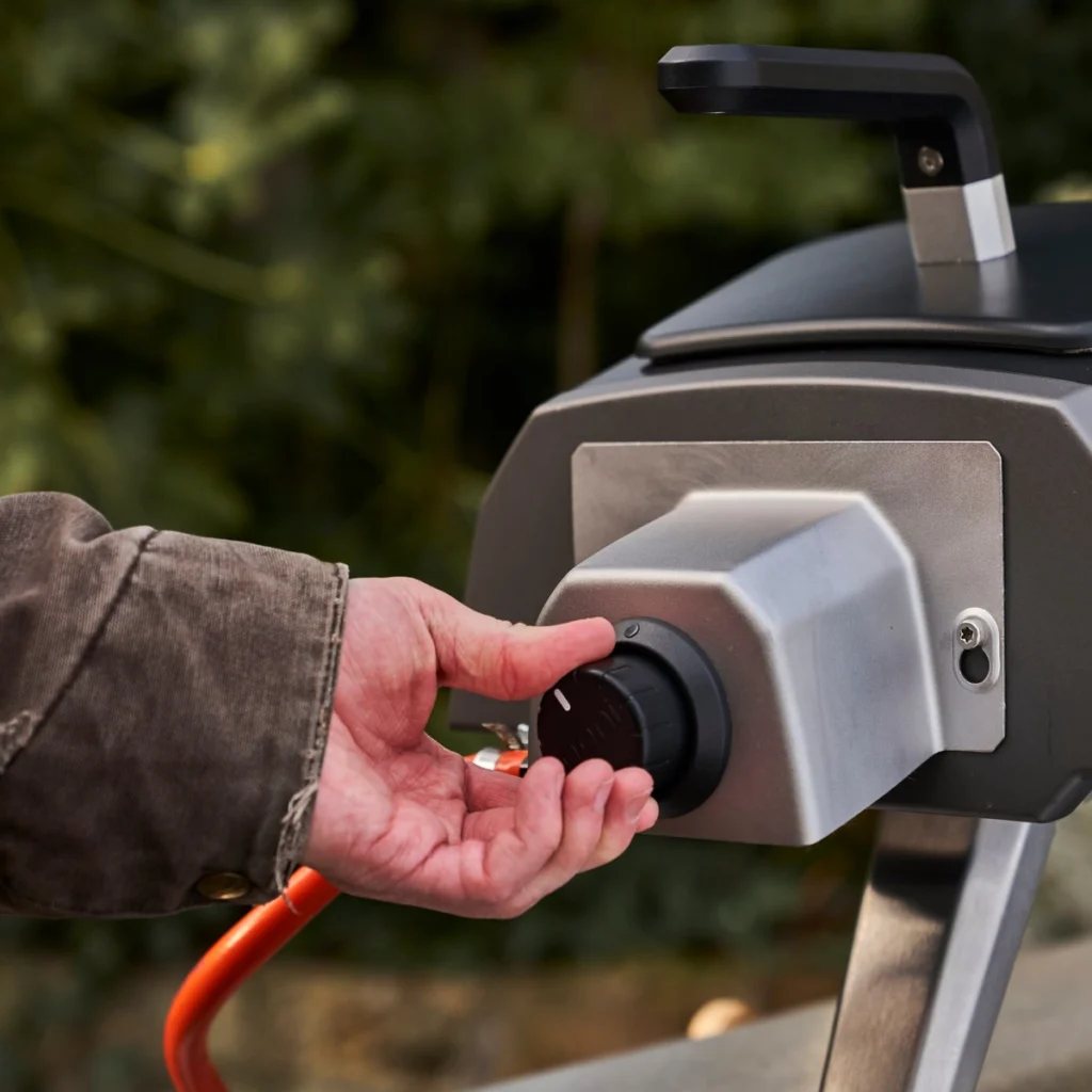 Une main règle le brûleur à gaz en option fixé à l’arrière de l’Ooni Karu 2