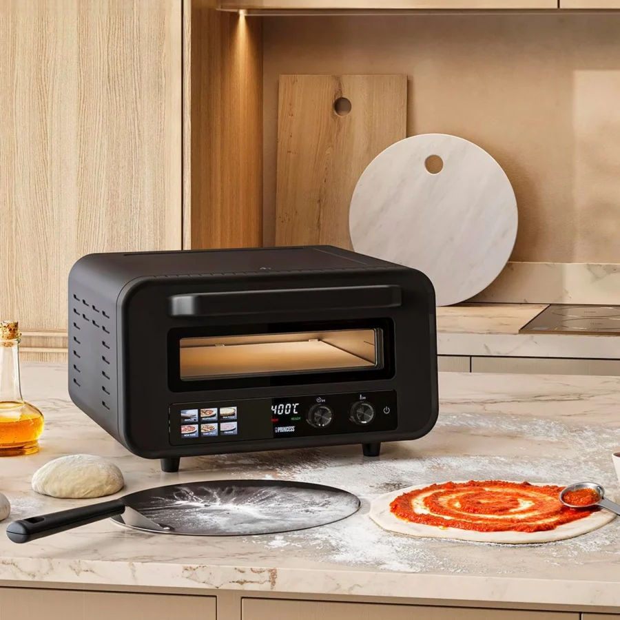 Princess 112780 sur le plan de travail d’une cuisine, une pâte à pizza garnie de sauce tomate et la pelle devant