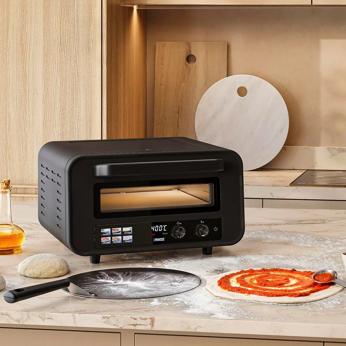 Princess 112780 sur le plan de travail d’une cuisine, une pâte à pizza garnie de sauce tomate et la pelle devant