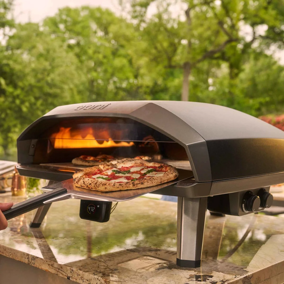 Ooni Koda 2 Max dans un jardin : deux pizzas en cuisson, une margherita sortie à la pelle