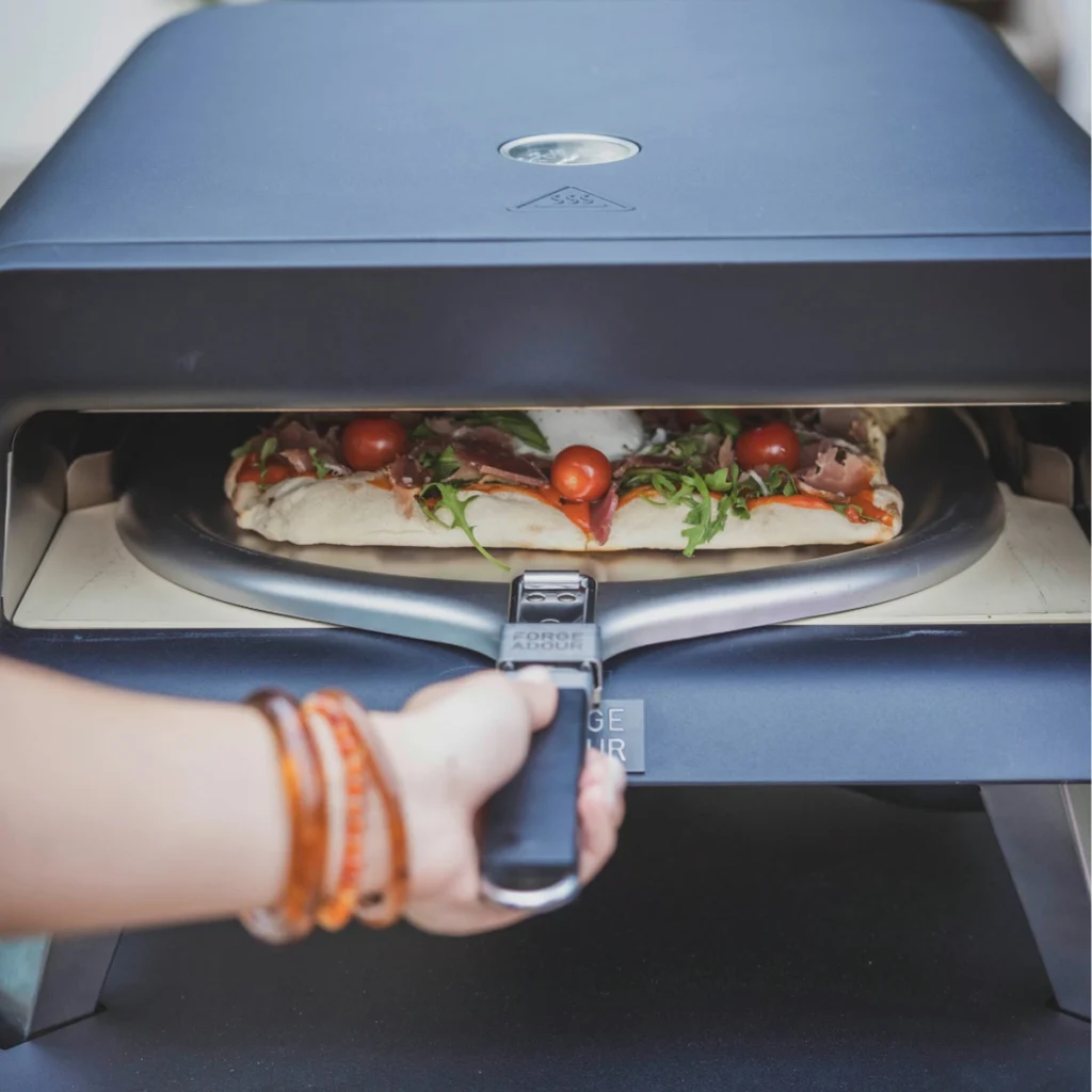 Une main enfourne une pizza dans le Forge Adour Pro avec la pelle Forge Adour