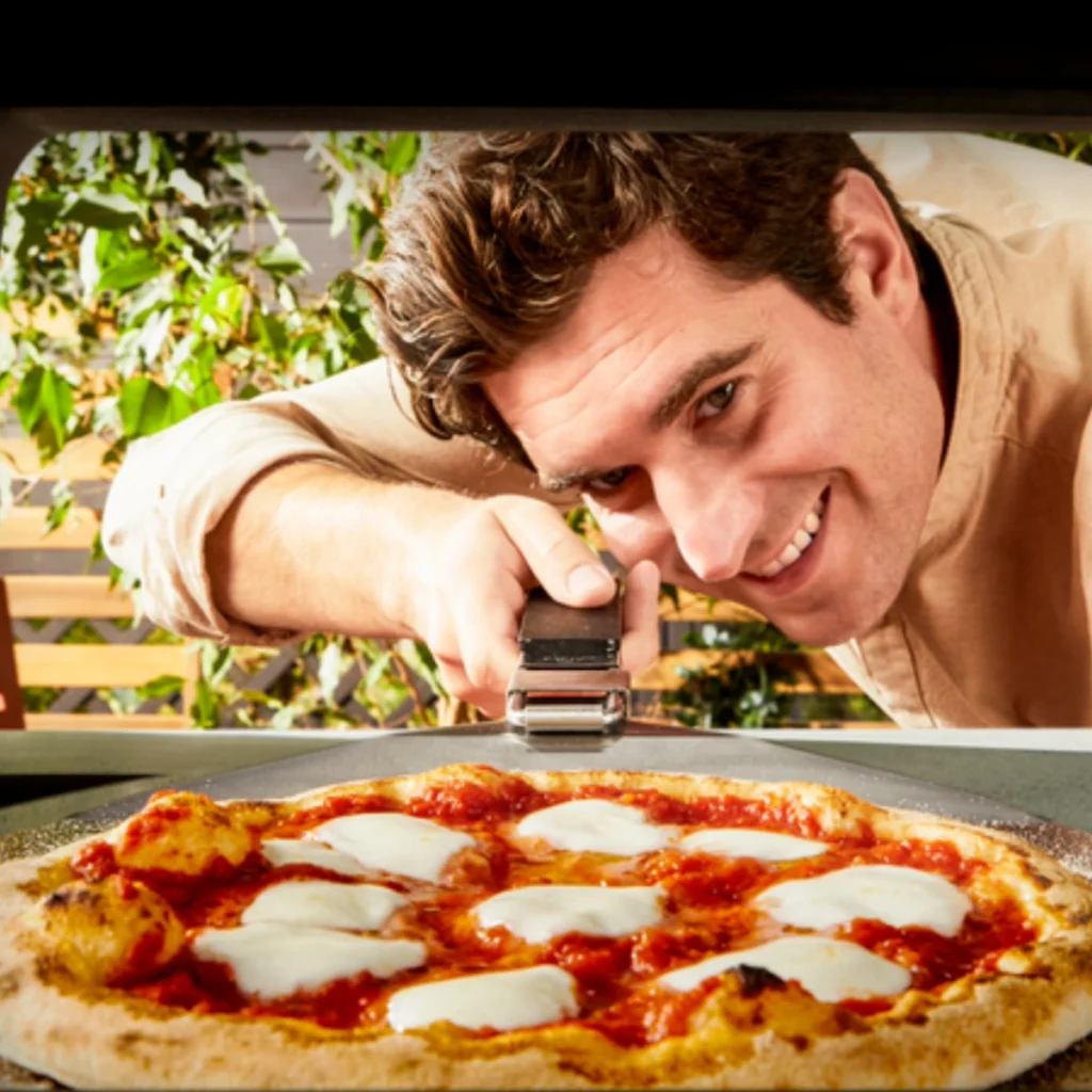 Vue depuis l’intérieur du Tefal Pizza Pronto Gaz : un homme enfourne une pizza margherita à la pelle