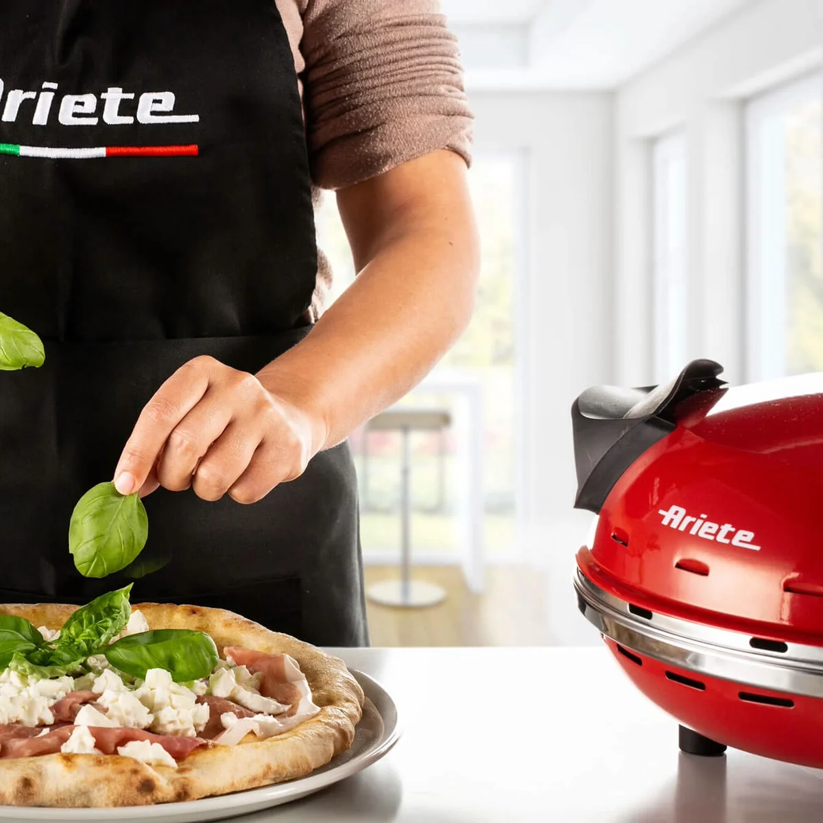 Une personne dépose du basilic sur une pizza, l’Ariete 909 à côté sur le plan de travail