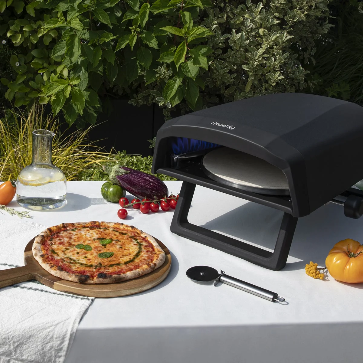 H.Koenig GINO640 allumé sur une table de jardin, une pizza margherita posée sur une planche