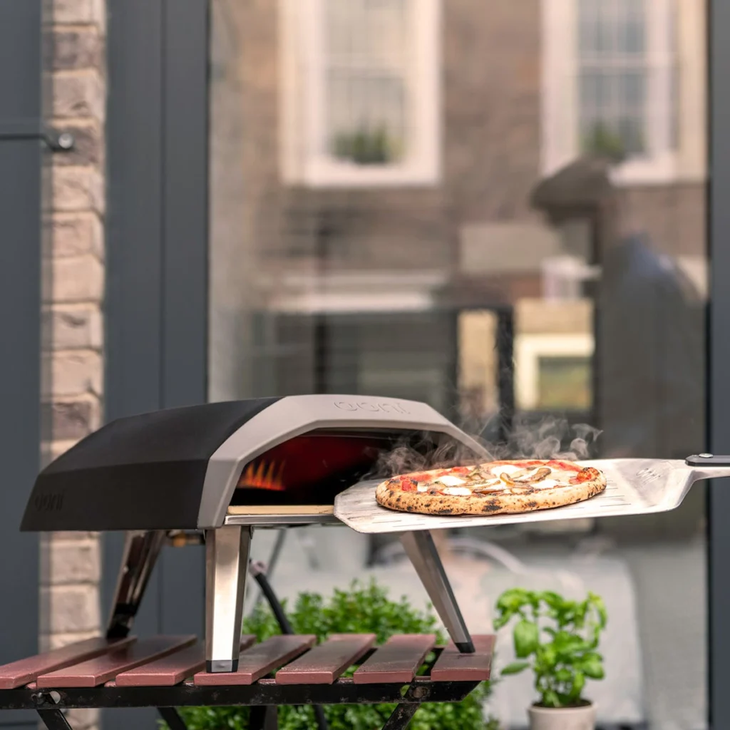 Ooni Koda 12 sur une table de jardin, une pizza fumante sur la pelle