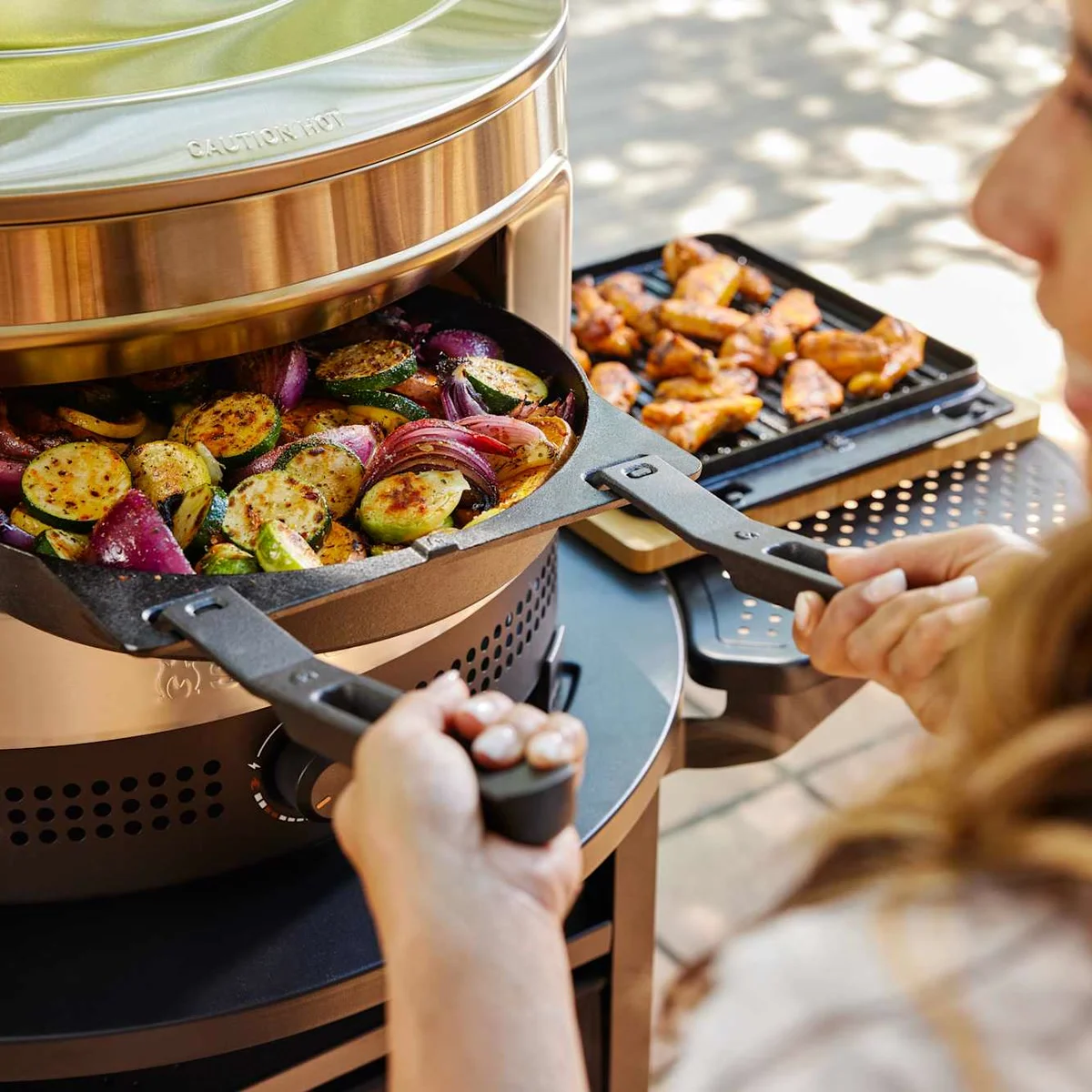 Une poêle de légumes rôtis sort du Solo Stove Pi Prime, des ailes de poulet à côté