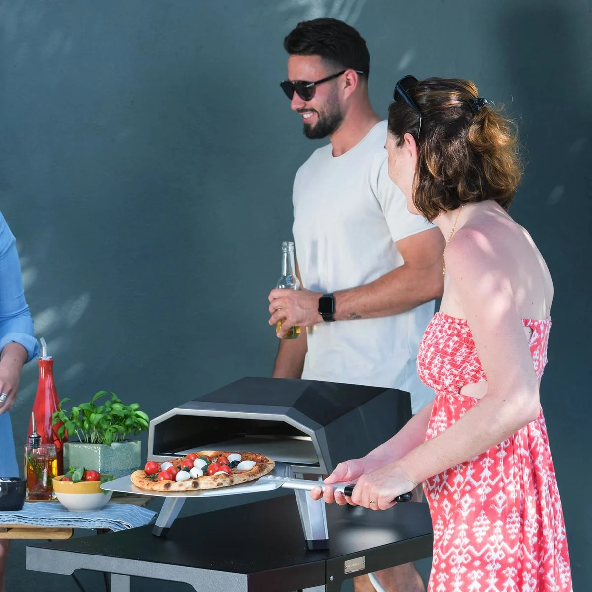 Une pizza tomates et mozzarella sur la pelle devant le four Le Marquier Duo 12", sur une terrasse entre amis