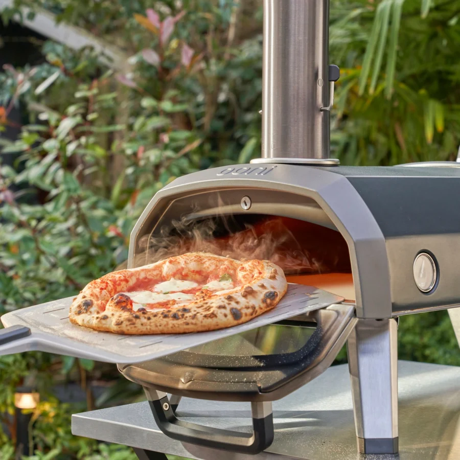 Une pizza margherita fumante sort de l’Ooni Karu 2 sur une pelle, dans un jardin
