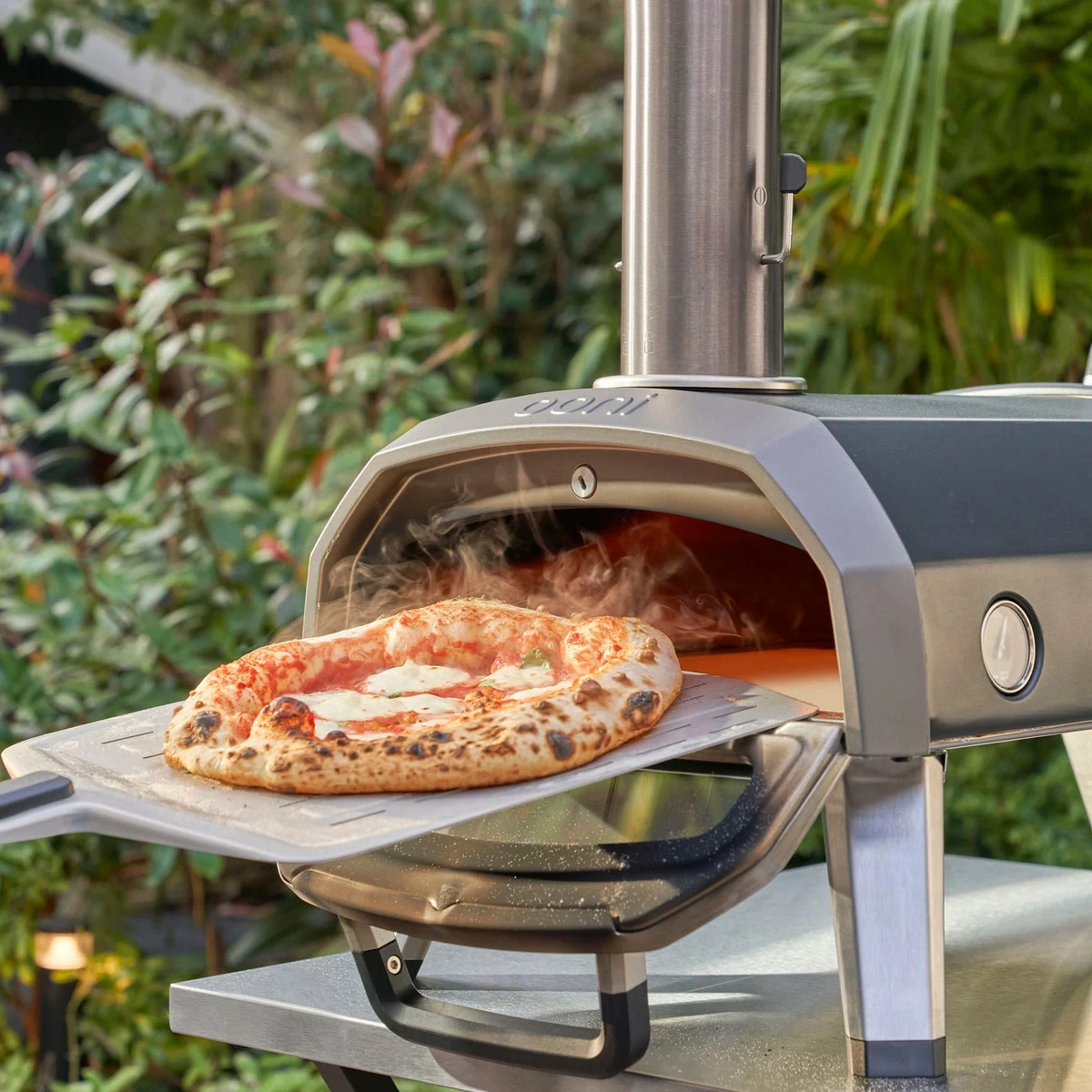 Une pizza margherita fumante sort de l’Ooni Karu 2 sur une pelle, dans un jardin