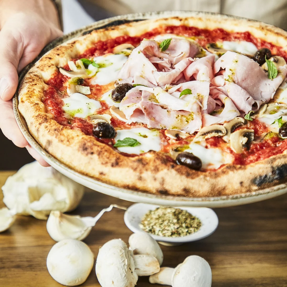 Une pizza jambon, champignons et olives cuite au four à pizza