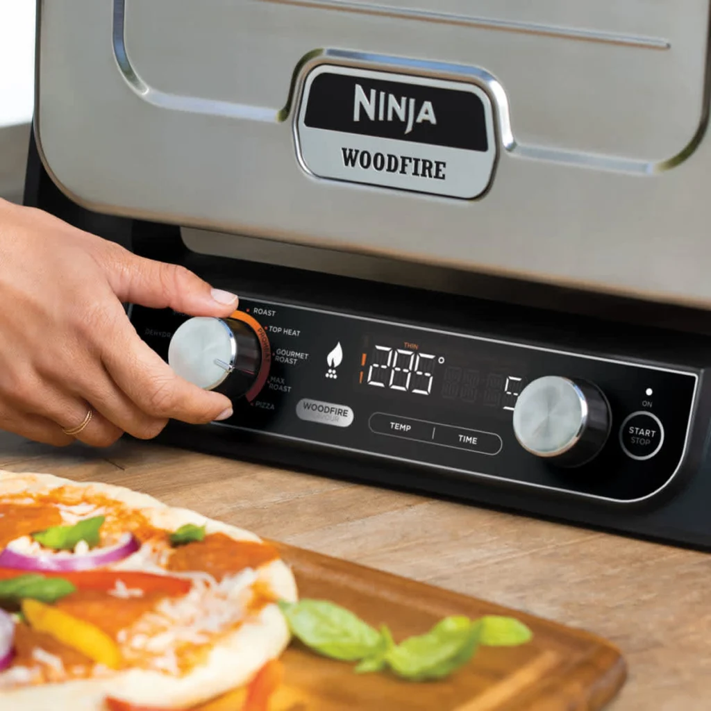 Une main règle la température du Ninja Woodfire, une pizza prête à enfourner devant