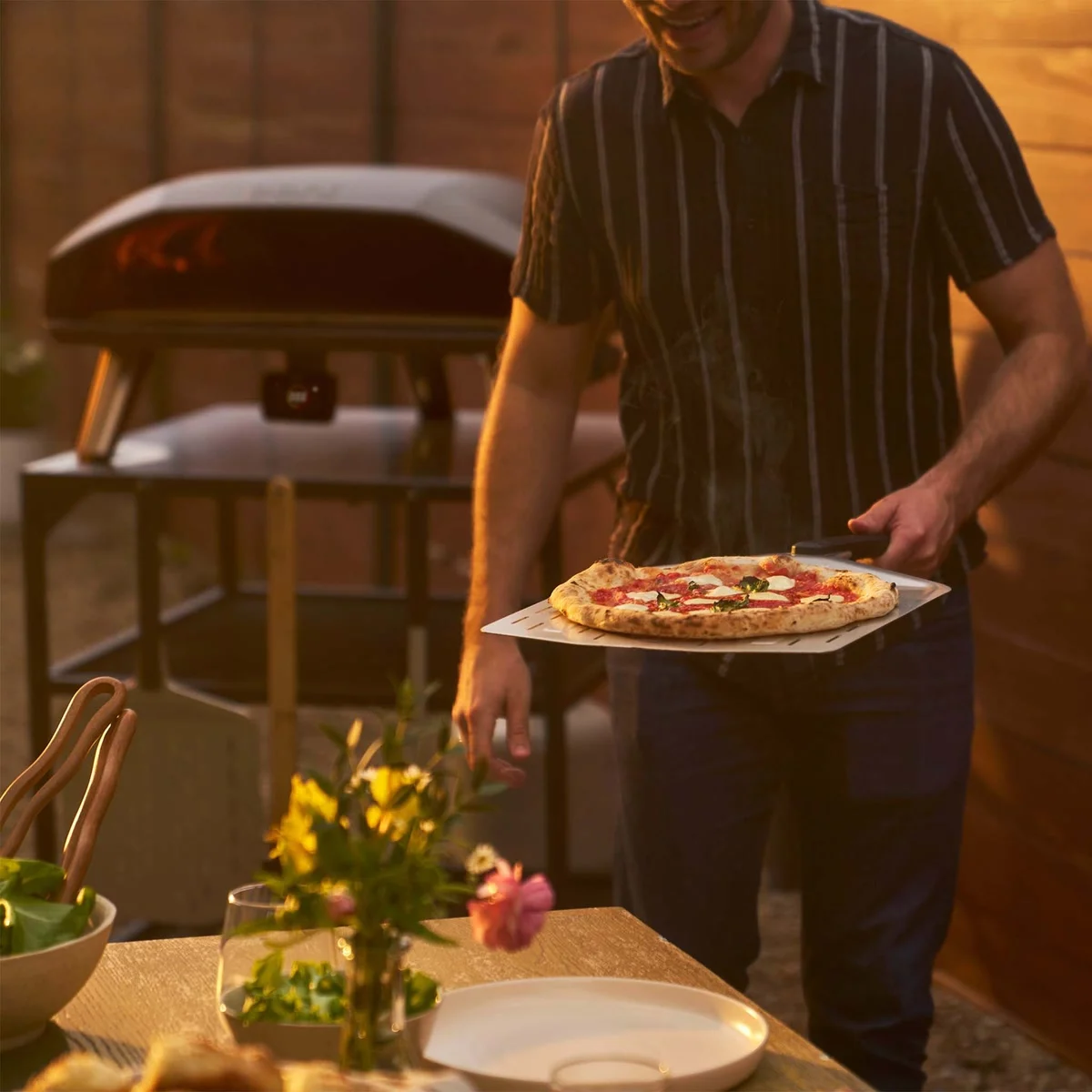 Une pizza margherita sortie de l’Ooni Koda 2 Max apportée à table au coucher du soleil