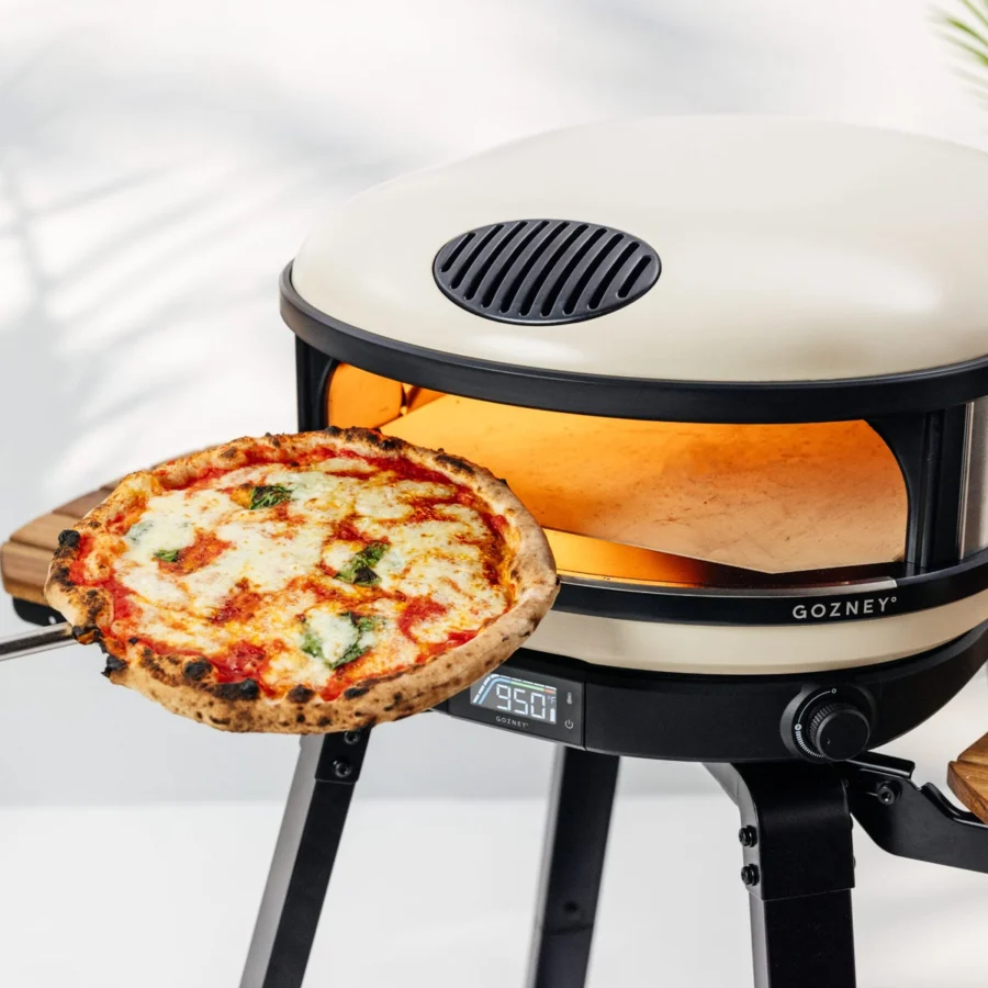 Une pizza margherita sort du Gozney Arc XL crème à la pelle, le four allumé sur son support