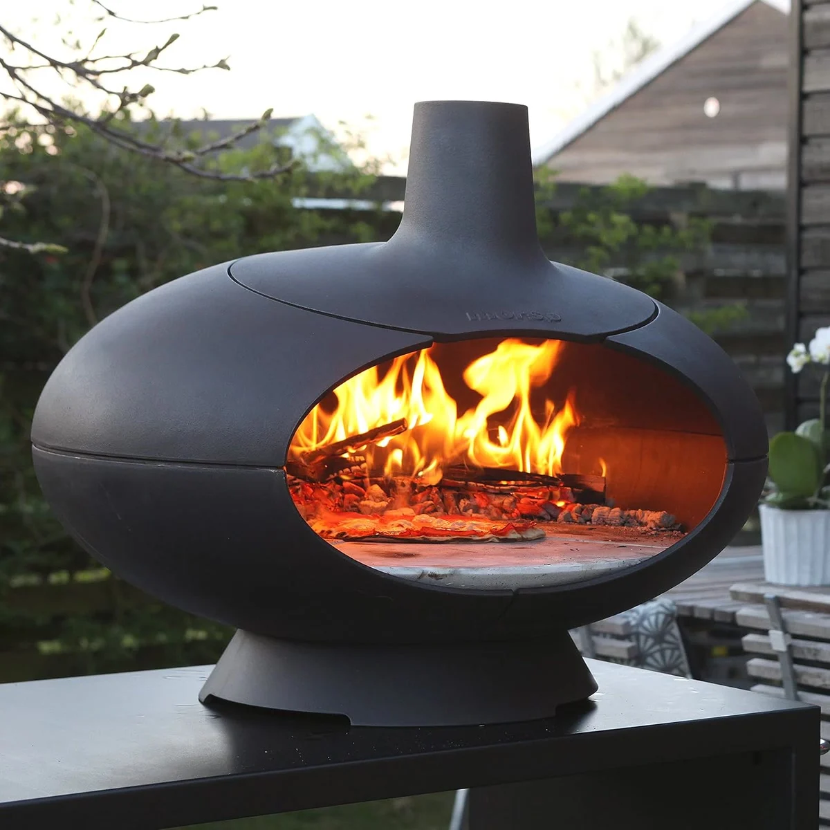 Morsø Forno allumé sur une terrasse en fin de journée, une pizza cuit devant les flammes