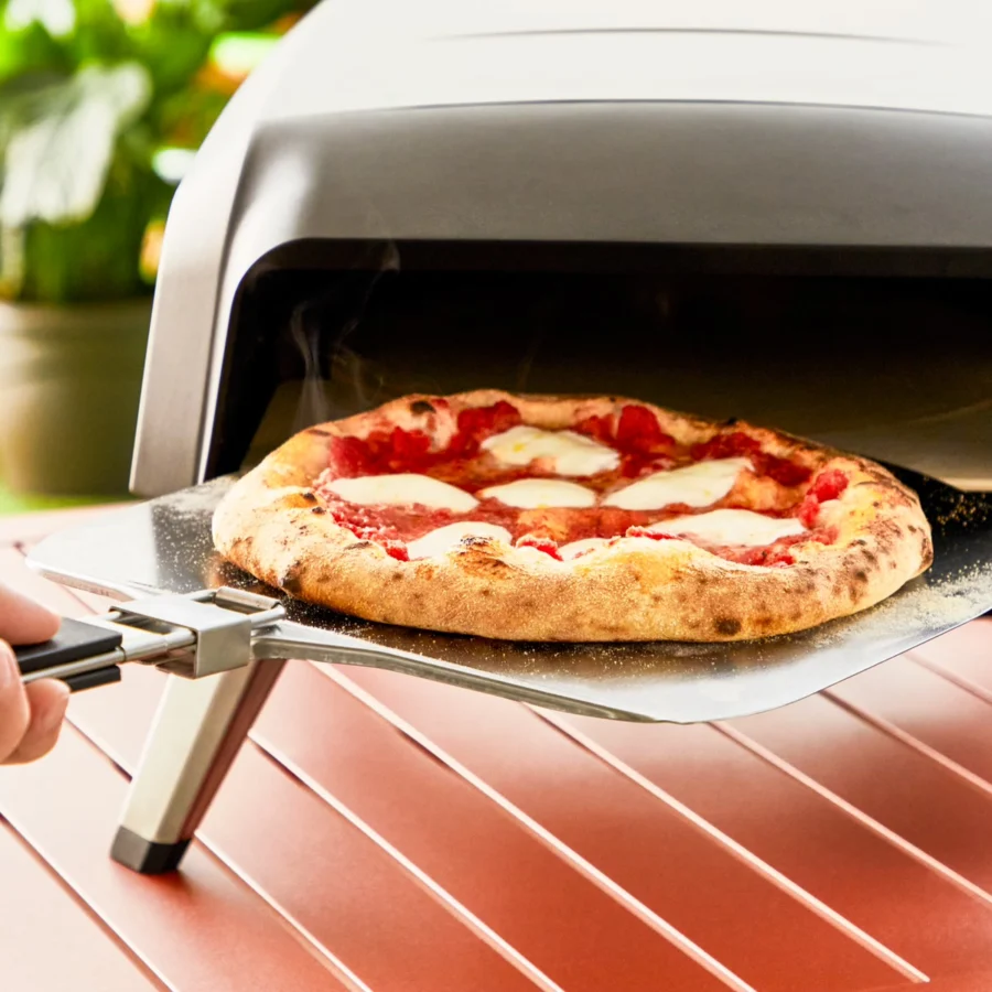Une pizza margherita sort du Tefal Pizza Pronto Gaz sur sa pelle, sur une table de jardin