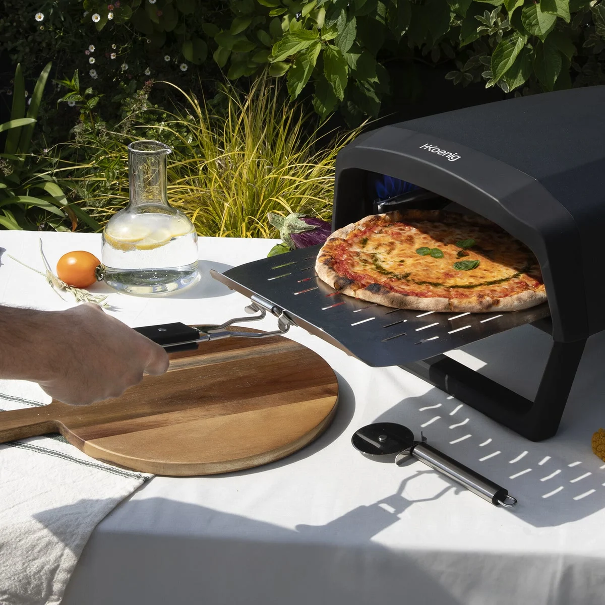 Une pizza margherita sort du H.Koenig GINO640 sur sa pelle perforée, sur une table de jardin